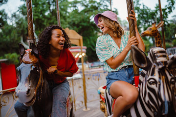 Young multiracial women riding on carousel in attraction park