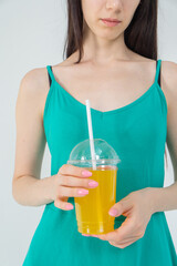 The hands of a girl in a green dress hold a glass of juice: close-up