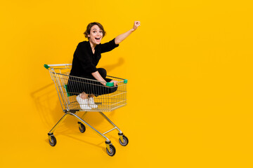 Photo of impressed funny lady wear black shirt riding shopping tray rising fist empty space...