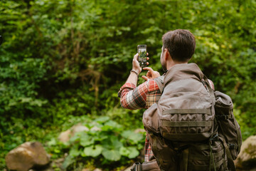 Happy white man taking photo on cellphone while hiking in forest