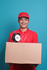 Delivery man in red uniform work as dealer courier hold a blank cardboard box with a clock. Courier delivering quickly on time concept