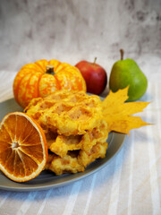 Belgian gluten-free pumpkin waffles lie on a gray plate with a dry slice of lemon and anise stars, pumpkin, apples on a gray and white tablecloth, veganism. side view