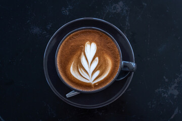 Hot coffee latte with latte art milk foam in cup mug on black wood desk on top view. As breakfast In a coffee shop at the cafe,during business work concept