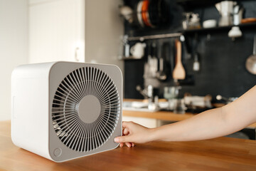 autumn concept and technology. A woman's hand turns on an air heater in an apartment against the backdrop of a cozy interior.