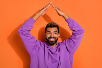 Photo of funky nice dude boy model stylish pullover hold arms over head make house roof isolated on orange color background.