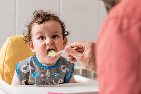 Unrecognizable father feeding infant son with cereals at home