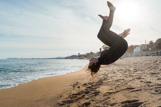 Young Woman In Wetsuit Doing Trick On Beach