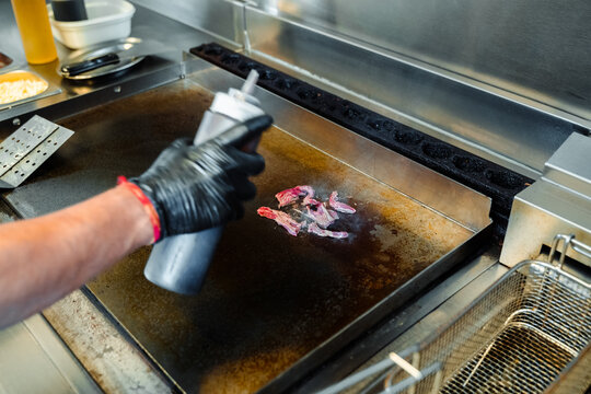 Crop chef with squeeze bottle frying beef slices in kitchen