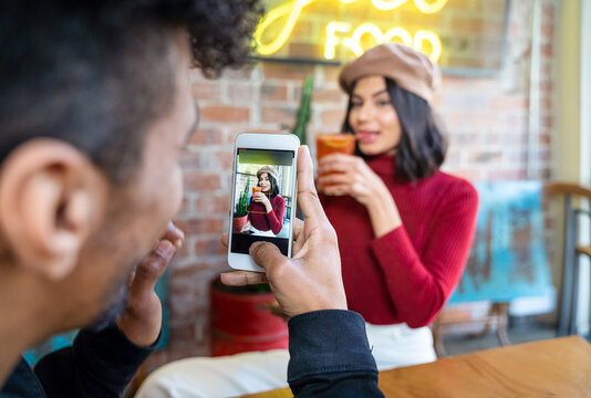 Man taking photo of cheerful girlfriend with glass of cocktail