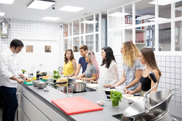Attentive multiracial students listening explanation of professional chef at cooking workshop