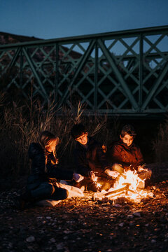 group of young friends camping and burning a wood fire under a bridge