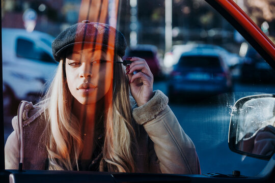 Ethnic female applying makeup near car
