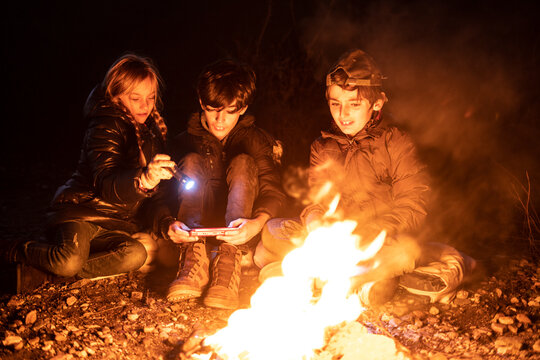 Young friends camping near fireplace with mobile phone
