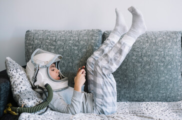 Kid lying on couch and playing with a video game console at home