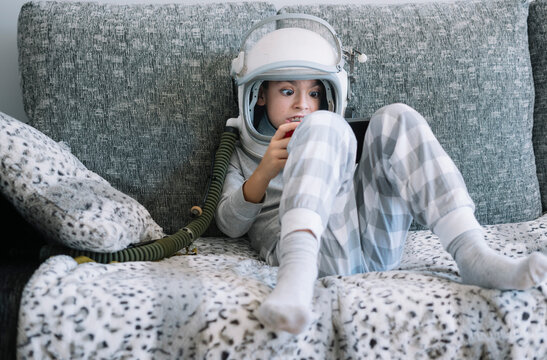 Kid lying on couch and playing with a video game console at home