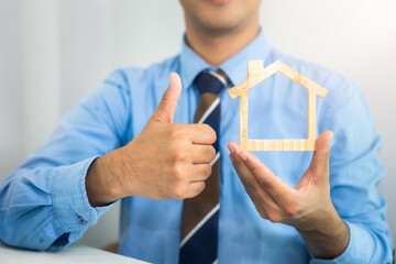 Businessman, agent or broker at front. To hold model of home, house or residential building in hand...