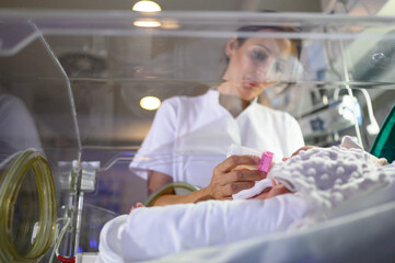 Nurse feeding baby in incubator