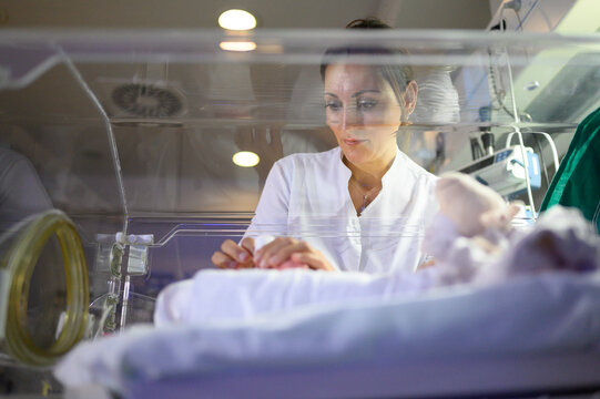 Nurse gently touching fragile newborn in neonatal incubator