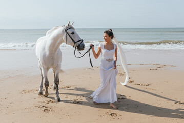 Smiling bride with horse walking on sea beach