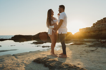 Pregnant couple standing near sea at sunrise
