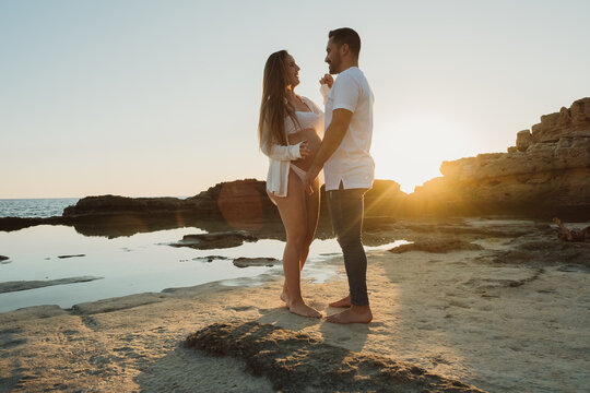 Pregnant couple standing near sea at sunrise