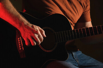 Man Playing Guitar with Neon Light. Unrecognizable Person Rehearsing. Strumming Acoustic Guitar. Musician Plays Music. Male Fingers and Fretboard Close Up. Man Hand Playing Guitar Neck in a Dark.