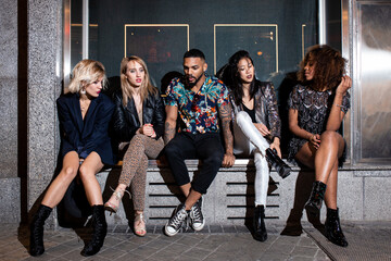 Stylish diverse friends sitting on street at party