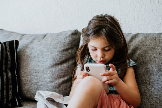 Cute Ethnic Child Using Smartphone On Cozy Couch At Home