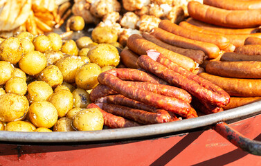 Appetizing grilled sausages and baked potatoes in a frying pan