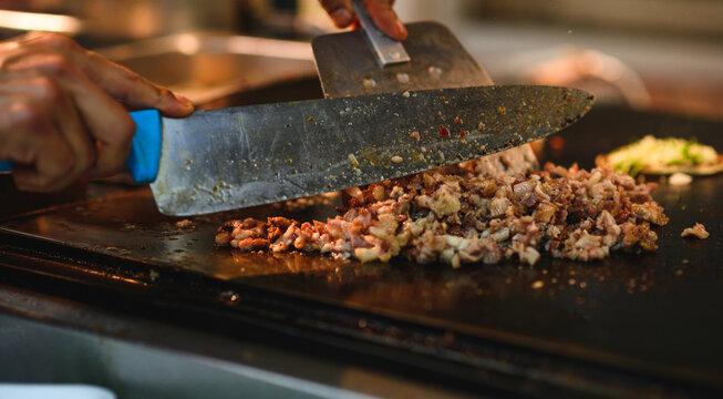 Crop cook chopping meat slices on griddle at work - Powered by Adobe