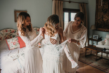 Cheerful women helping lady to clothe dress in bedroom