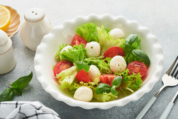 Caprese salad. Italian caprese salad with sliced tomatoes, mozzarella cheese, basil, olive oil in white plate over white background. Delicious Italian food. Top view. Rustic style.