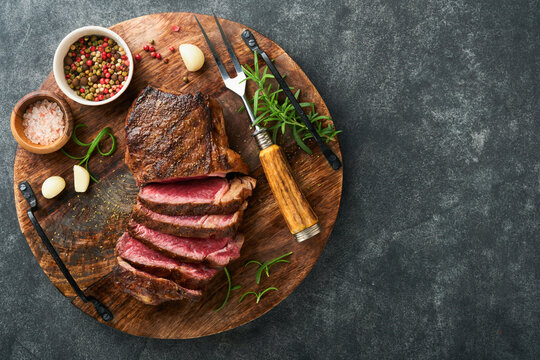 Steaks. Sliced grilled meat steak New York or Striploin with spices rosemary and pepper on black marble board on old stone grey background. Top view. Mock up.
