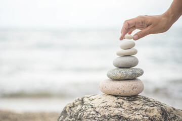 Tanned woman hands stacked pebble stones tower on sea beach relaxing harmony summer travel vacation