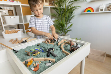 Cute baby boy playing sensory box kinetic sand table with farm animals