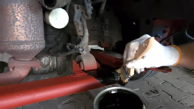 Maintenance of the old car chassis, hand-painted engine compartment of the sleds with a brush with a black anti-corrosion agent
