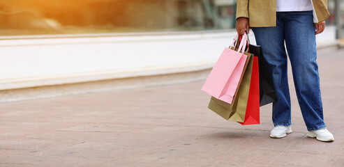Cropped of unrecognisable woman with colourful shopping bags on urban shopping mall background. Purchases, black friday, discounts, sale concept. Online shopping concept, Seasonal Sales. copy space