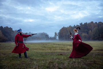 Duel of a man and a woman in 17th century costumes using antique pistols. Opponents aim at each other.