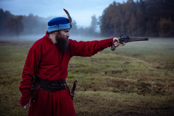 Bearded man in 17th century clothes and hat with antique pistol aiming from an old pistol, side view