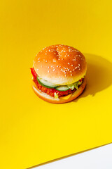 A burger with vegetables on a yellow background with space for text. Creative concept of food delivery.
