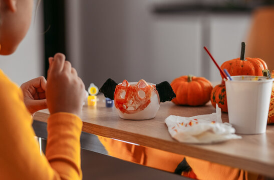 A little girl paints a clay hand made pumpkin. Halloween party. Crafts for children.