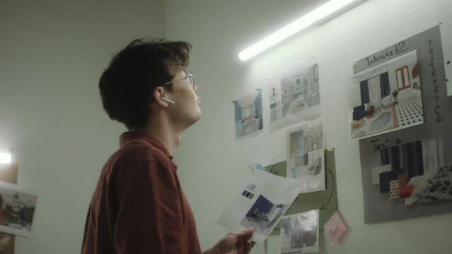 Gen Z Asian designer pinning printed interior design plan to wall while working in architectural office