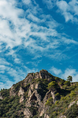 Fototapeta na wymiar Vegetation and trees on a rocky mountain under a blue cloudy sky.