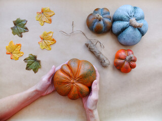 Female hands hold one of the artificial alabaster pumpkins on a beige background with rope and autumn leaves