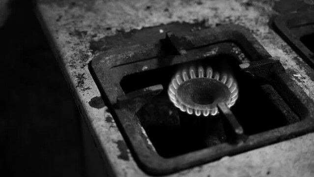 Unstable combustion of gas in the burner of an old gas stove in a deplorable state. A black and white video of a burning natural blue fuel in a rural slum. Low quality of life, poverty and heating