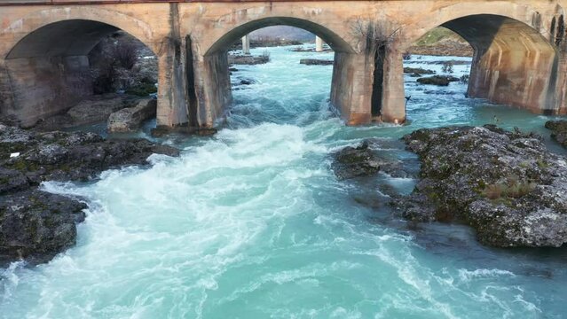 Blue river flowing under an arch bridge through beautiful rocky landscape. Aerial drone view of Cijevna (Cem, Cemi) stream in Montenegro, Europe.