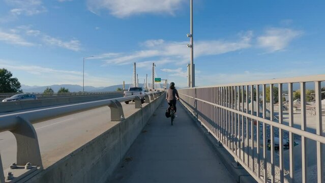 Woman Bike riding on a Bicycle Path over Golden Ears Bridge over the Fraser River. Pitt Meadows, Langley, Greater Vancouver, British Columbia, Canada. High quality 4k footage