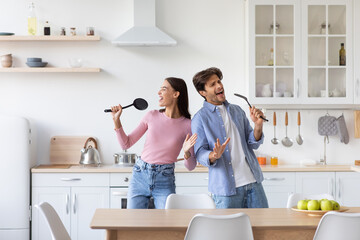 Carefree cheerful funny emotional young couple singing and dancing together in white kitchen
