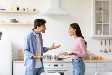 Fototapeta premium Angry offended young wife and husband shout, swear in kitchen interior. Couple arguing and conflicting