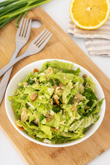 Chinese cabbage salad with green onion and seeds in white bowl on wooden board. Fresh vegetables slaw for healthy diet.
